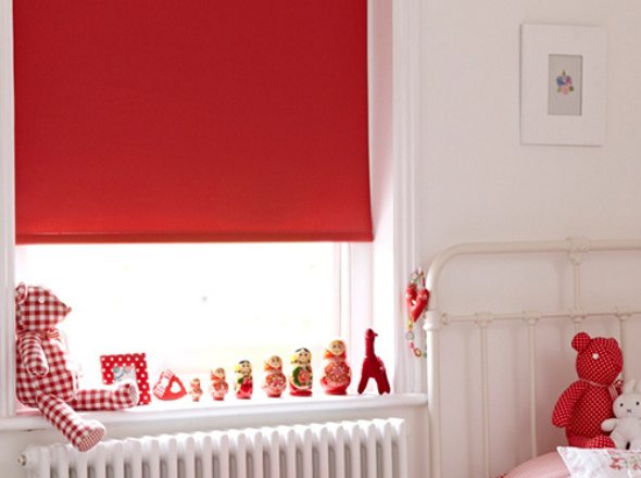 A bright red roller blind in a kids bedroom with red soft toys
