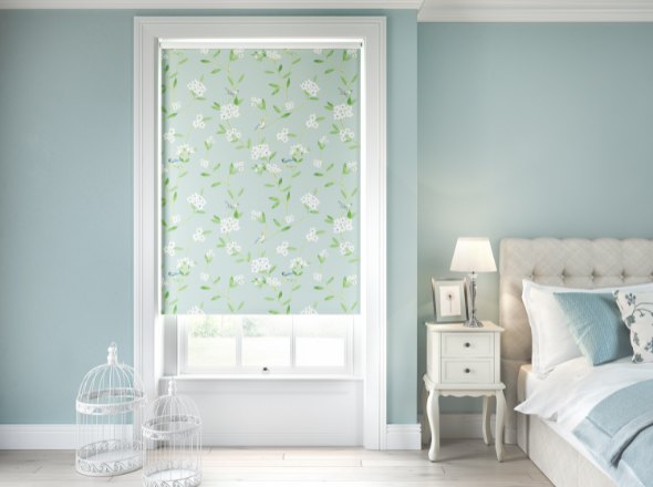 A blackout green patterned roller blind in a bedroom decorated in blue and white