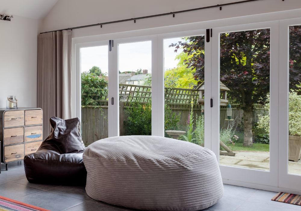 A white bifold door with an extra long curtain pole looking into a green garden