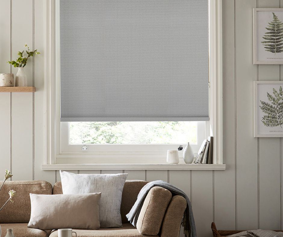 A grey roller blind in a cosy living room with brown leather couch